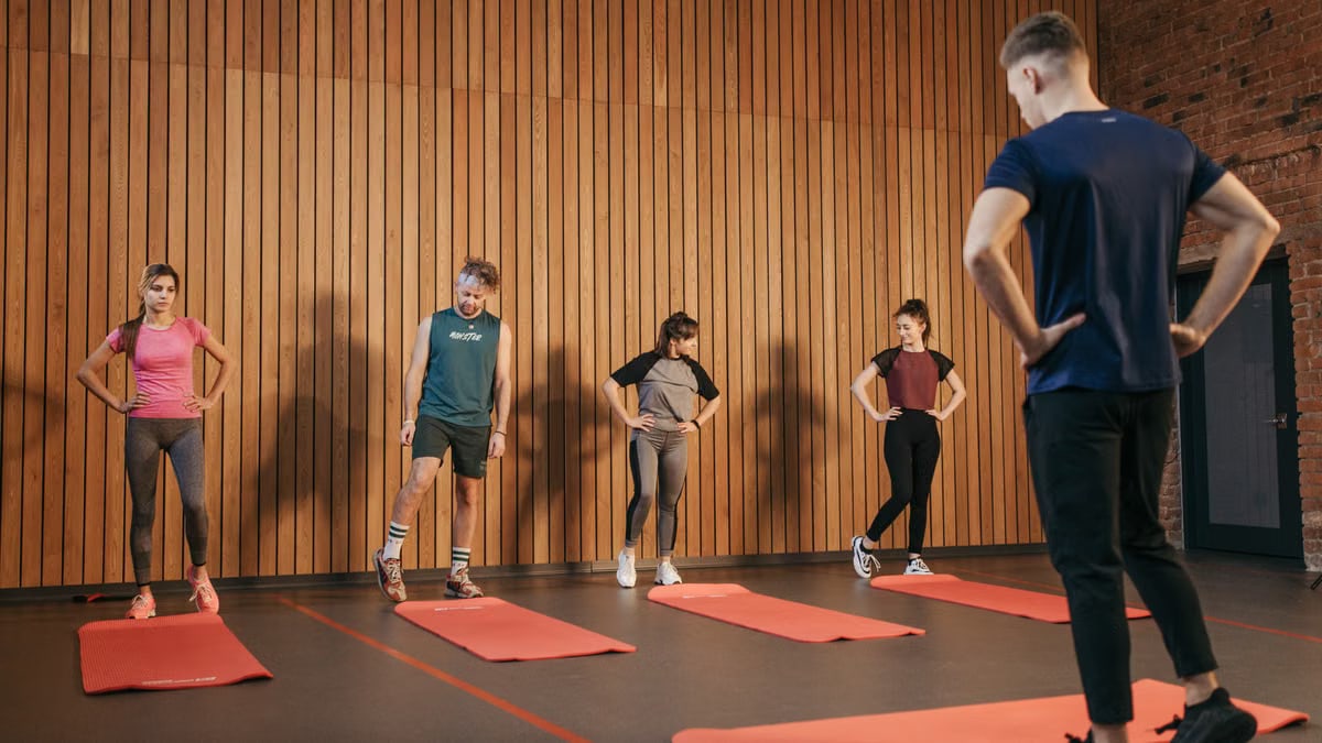 A group exercise class with a personal trainer leading stretching exercises in a gym.